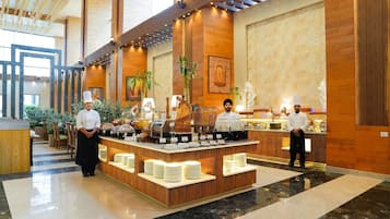 A buffet setup with chefs, a marble floor, wooden paneling, and a large window.