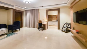 A modern hotel room with a large TV, a desk with a chair, a dining area, and a large window. - The Meriton (New Delhi)