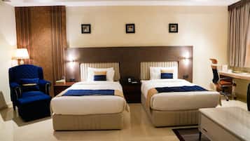 A hotel room with two beds, a chair, a desk, and a lamp.