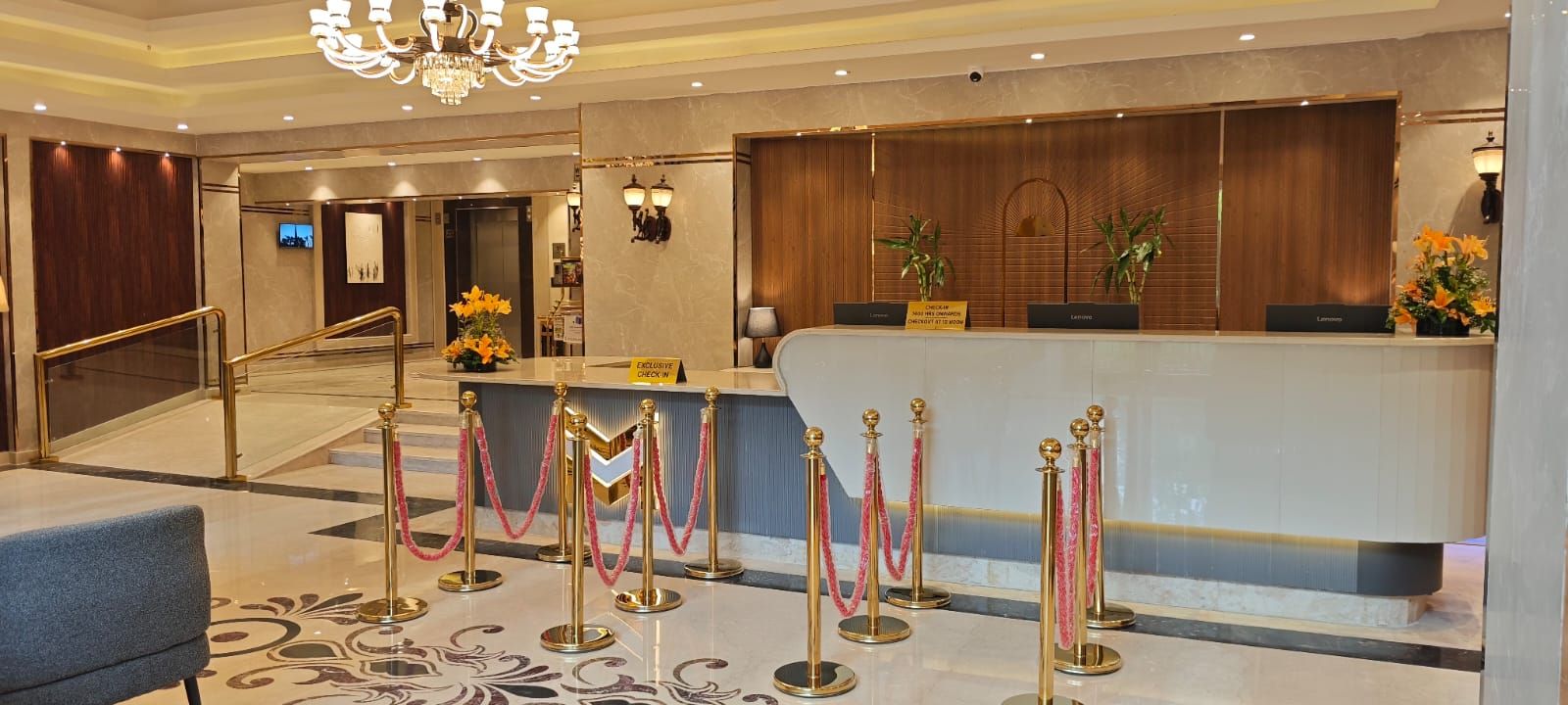 A hotel reception area with a marble floor, a reception desk, and a staircase leading to another floor.