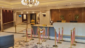 Zona de recepción de hotel con suelo de mármol, un mostrador de recepción y una escalera que sube a otro piso.