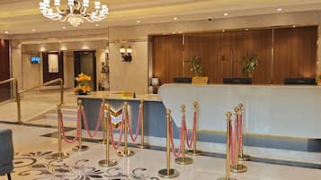 A hotel reception area with a marble floor, a reception desk, and a staircase leading to another floor.