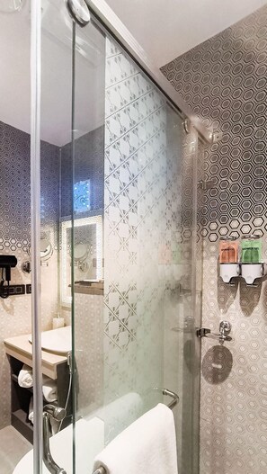 A modern bathroom with a glass shower enclosure, a vanity with a mirror, and a toilet. - The Meriton (New Delhi)