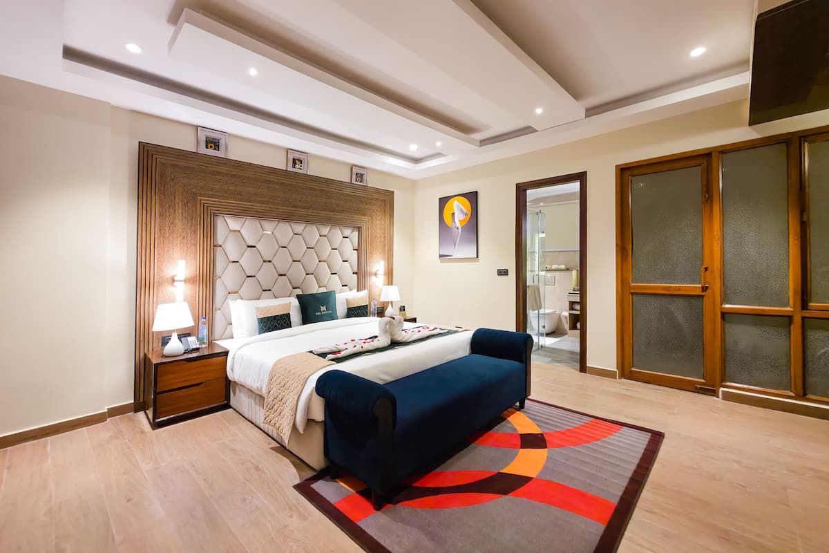 A modern hotel room with a large bed, a bedside table with a lamp, a blue sofa, and a colorful rug.