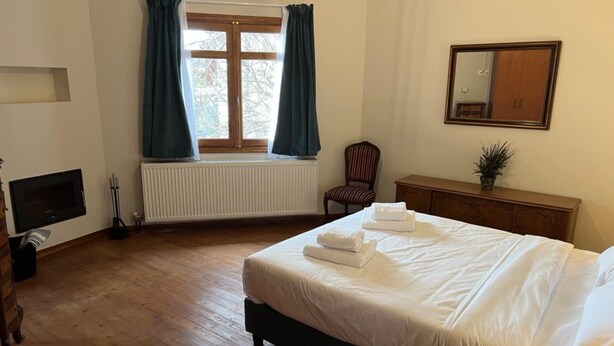 A bedroom with a bed, a dresser, a chair, a radiator, a window with curtains, and a mirror on the wall. - Aurora Inn (Volos)