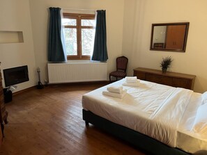 Una camera da letto con un letto, una cassettiera, una sedia, un termosifone, una finestra con tende e uno specchio a parete.