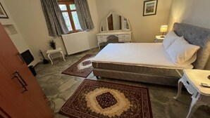 A bedroom with a large bed, a dresser, a nightstand, a lamp, and a window with curtains. - Aurora Inn (Volos)