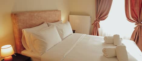 A neatly made bed with white linens and pillows, a bedside lamp, and a window with curtains.