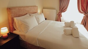 A neatly made bed with white linens and pillows, a bedside lamp, and a window with curtains. - Aurora Inn (Volos)