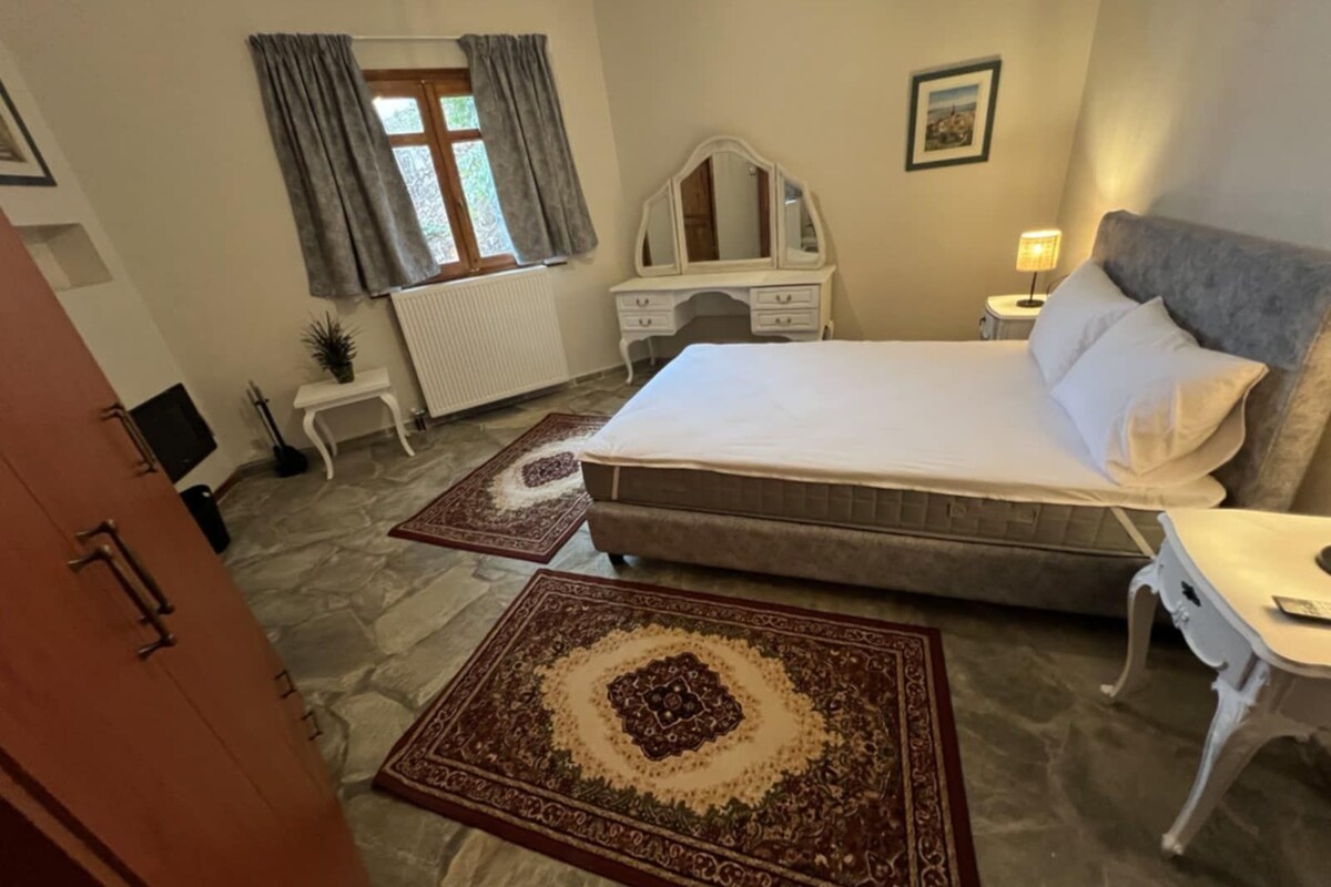 Una camera da letto con un letto grande, una cassettiera, un comodino, una lampada e una finestra con tende.