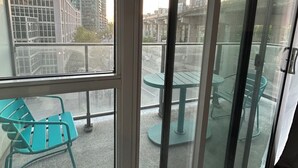 Un balcon donnant sur des immeubles de grande hauteur, une petite table et une chaise.