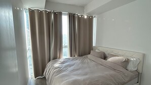 Une chambre moderne avec un grand lit, une table de chevet intégrée et une fenêtre avec des rideaux.