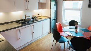 A modern kitchen with white cabinets, a black countertop, and a dining area with orange chairs. - Fabian Road Cozy House - Central London (London)