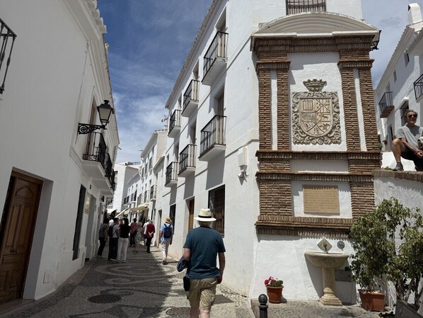 A narrow street lined with white buildings, some with balconies and decorative elements.
