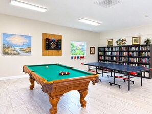Una habitación con mesa de billar, mesa de ping pong, dardos y una estantería con obras de arte.