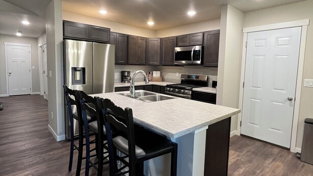 A modern kitchen with dark wood cabinets, stainless steel appliances, and a central island with bar stools. - Charming 3-bedroom home away from home in Rapid City! (Rapid City)