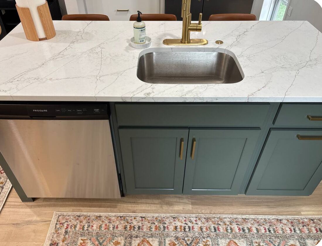 Ett kök med en inbyggd diskmaskin, en diskho med ett guldfärgat blandare och turkosa skåp.