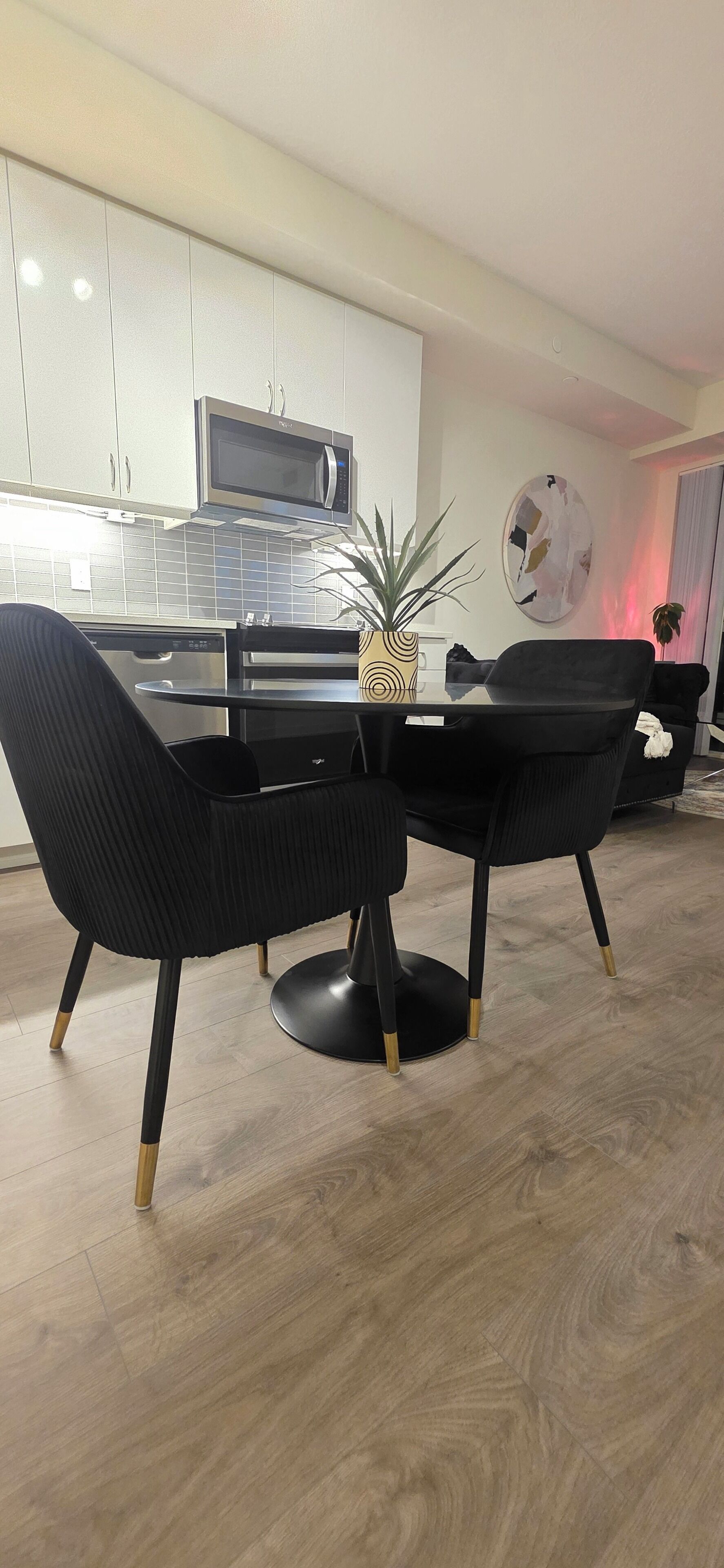 A modern kitchen with white cabinets, a built-in microwave, and a dining area with a black table and chairs.