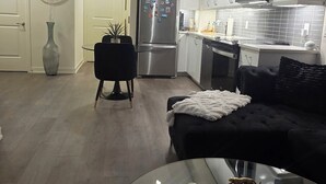 Eine moderne Küche mit Edelstahlgeräten, ein Essbereich mit einem Glastisch und ein Wohnzimmer mit einer schwarzen Couch und einem gemusterten Teppich.