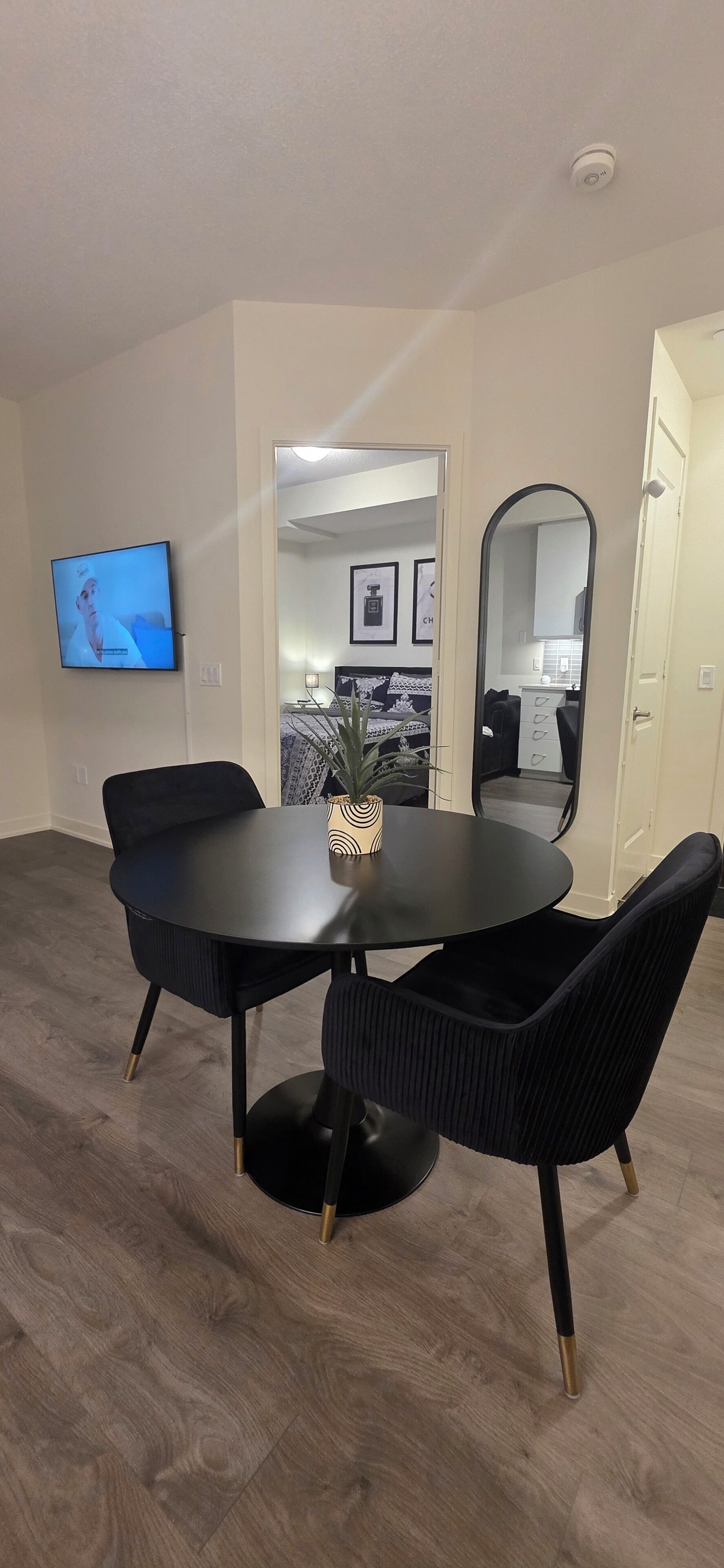 A modern living room with a round black table and matching chairs, a mounted TV, and a large mirror.