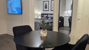 Ein modernes Wohnzimmer mit einem runden schwarzen Tisch und passenden Stühlen, einem Wand-Fernseher und einem großen Spiegel.