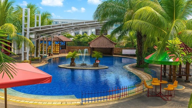 Una piscina con fuente, rodeada de palmeras y una zona de estar cubierta.