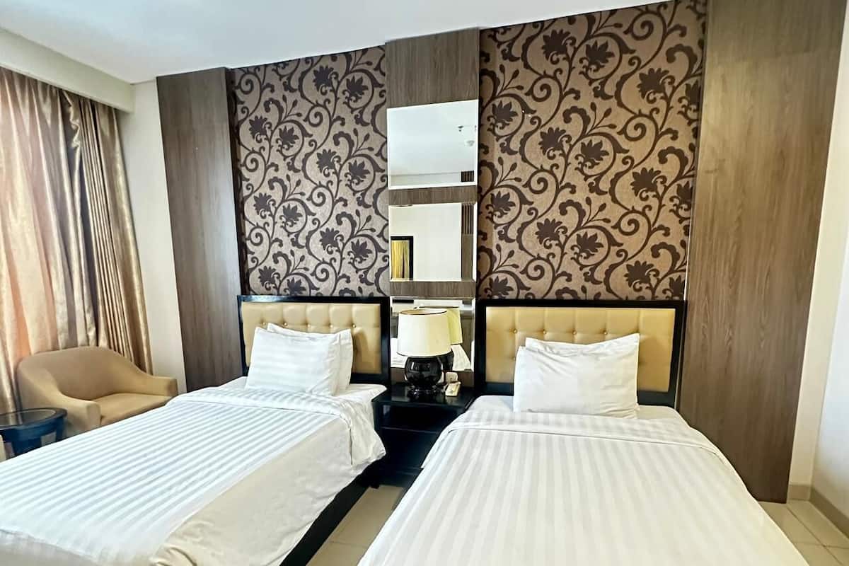 A hotel room with two beds, a chair, a lamp, and a mirror.