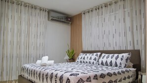 A modern bedroom with a large bed, white curtains, a potted plant, and a nightstand. - 3-bedroom apartment in peaceful San Francisco de Macorís with AC (San Francisco de Macorís)