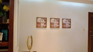 A hallway with three framed artworks on the wall, a wooden sculpture on a pedestal, and a door on the right. - 3-bedroom apartment in peaceful San Francisco de Macorís with AC (San Francisco de Macorís)