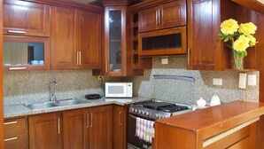 A kitchen with wooden cabinets, a granite countertop, a stove, a microwave, and a vase with flowers. - 3-bedroom apartment in peaceful San Francisco de Macorís with AC (San Francisco de Macorís)