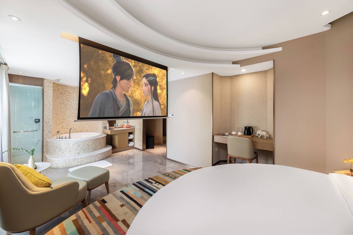 Ein modernes Badezimmer mit einer großen Badewanne, einer Dusche und einem Waschbecken. An der Wand ist ein Flachbildfernseher angebracht, und es gibt ein Sofa mit einer Tagesdecke.
