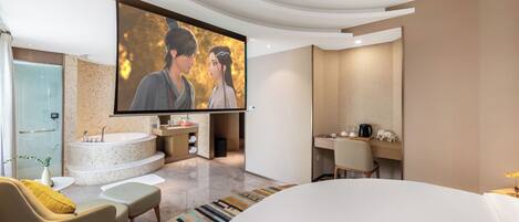 A modern bathroom with a large bathtub, a shower, and a sink. There is a flat-screen TV mounted on the wall, and a sofa with a throw blanket.