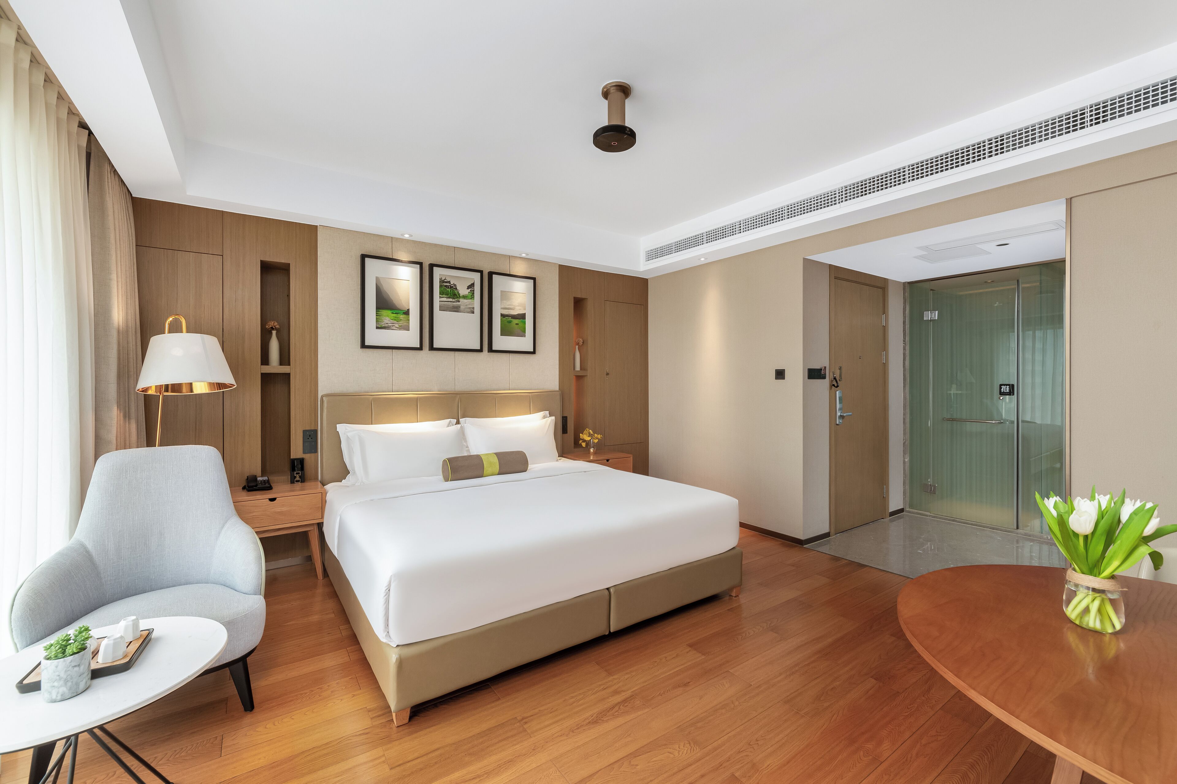 Een moderne hotelkamer met een groot bed, een bureau, een stoel, een kleine tafel met een plant en een vaas met bloemen.