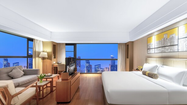 A modern hotel room with a city view, a bed, a sofa, a coffee table, and a TV. - Chengdu Yueming Hotel (Chengdu)