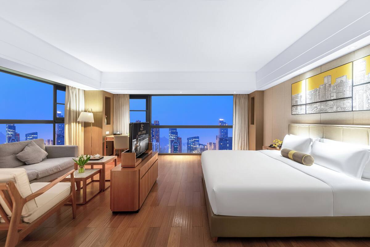 Ein modernes Hotelzimmer mit Blick auf die Stadt, inklusive Bett, Sofa, Couchtisch und Fernseher.