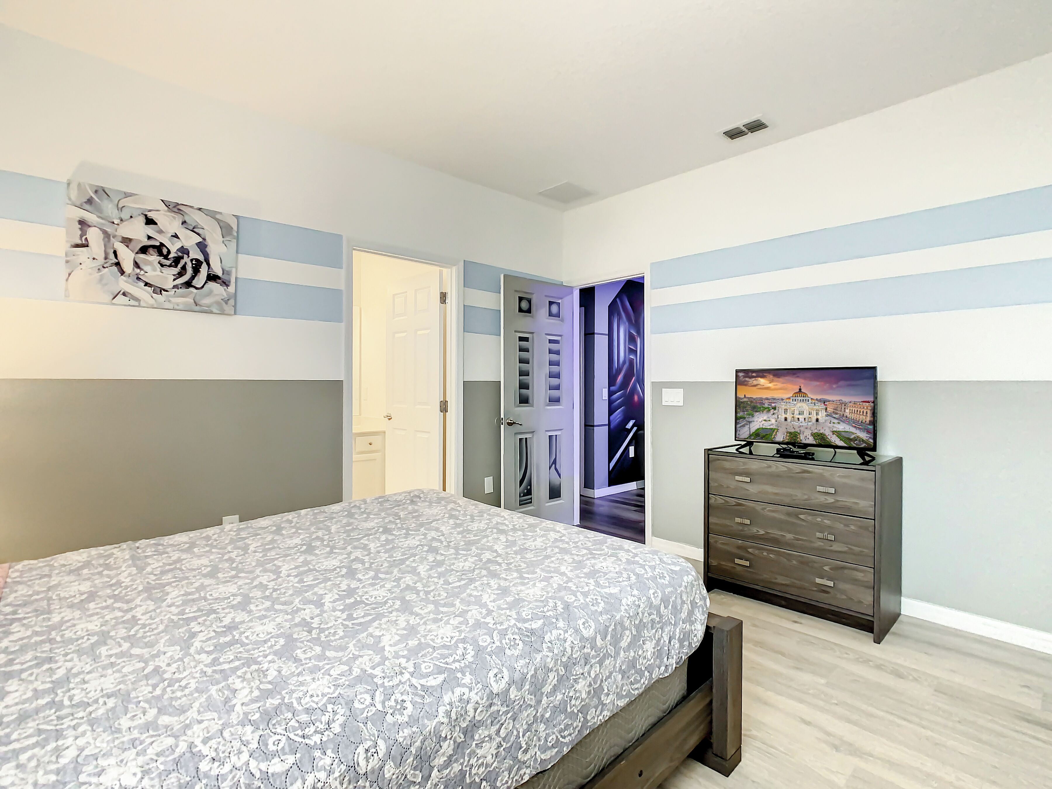 A bedroom with a bed, a dresser, and a door leading to another room.