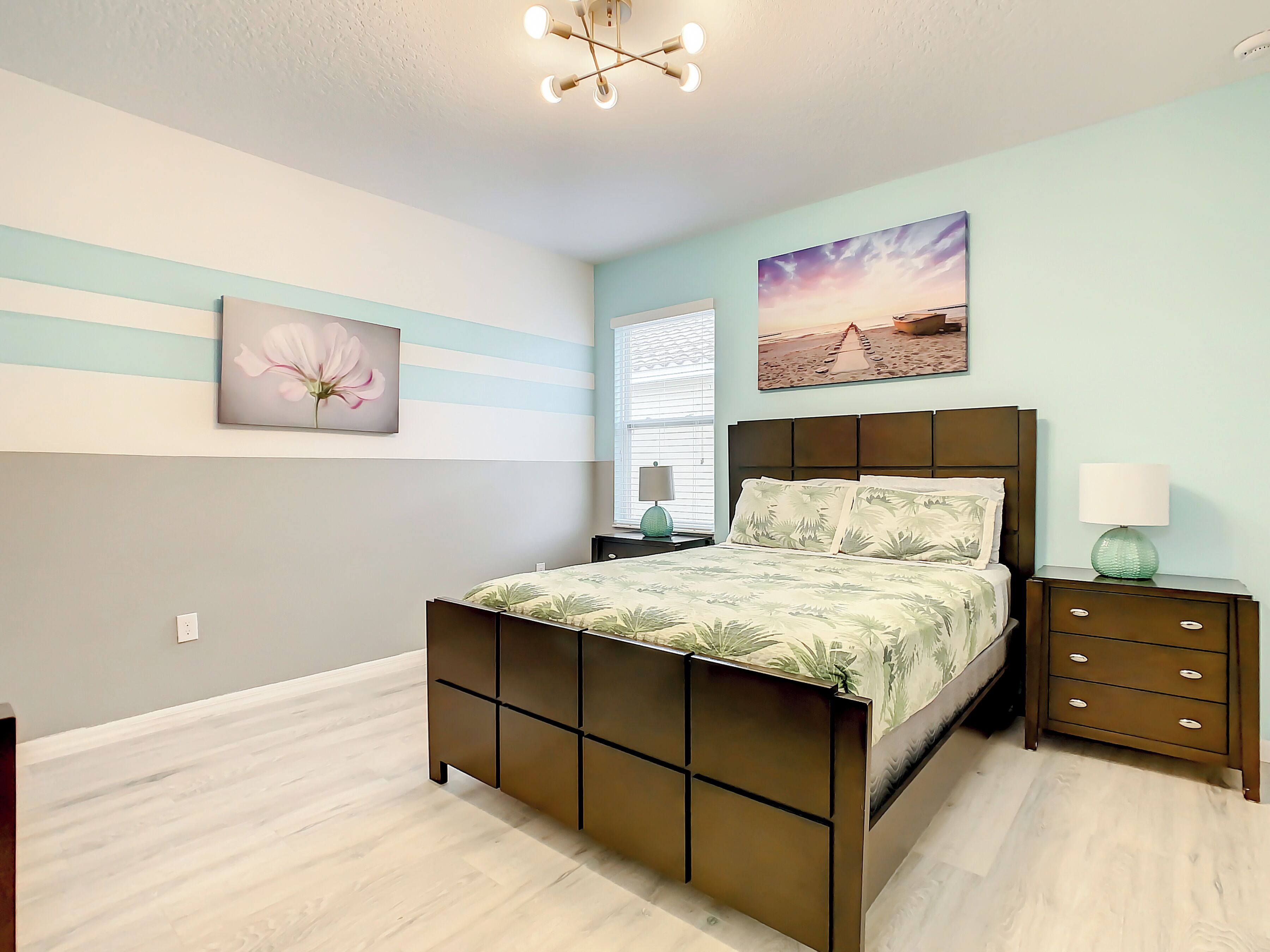 Un dormitorio con cama, mesitas de noche, lámpara y cuadros en la pared.