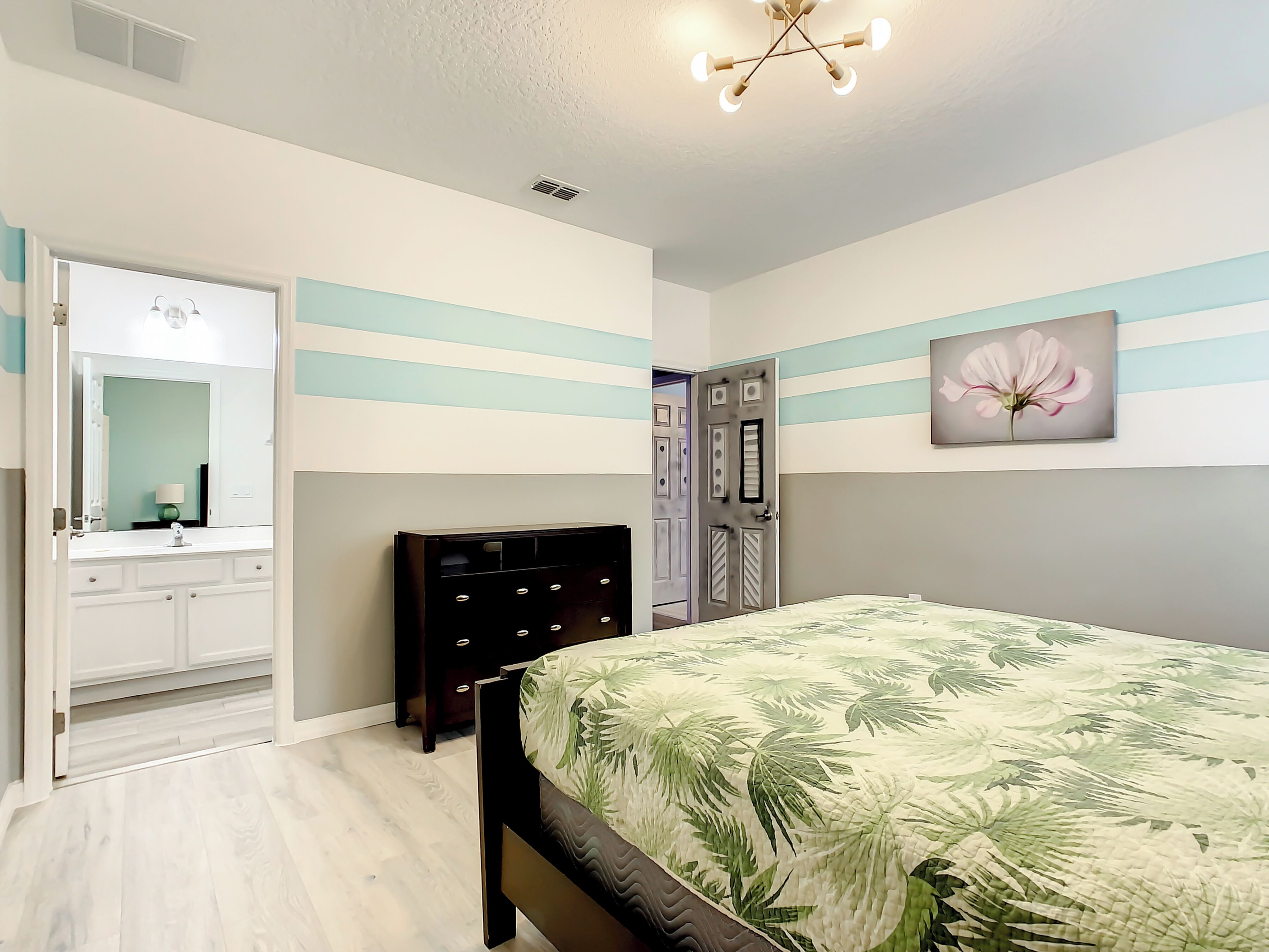 Een slaapkamer met een bed, een dressoir, een spiegel en een deur.