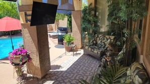 Un patio couvert avec une piscine, des sièges d’extérieur et un téléviseur fixé sur un pilier.