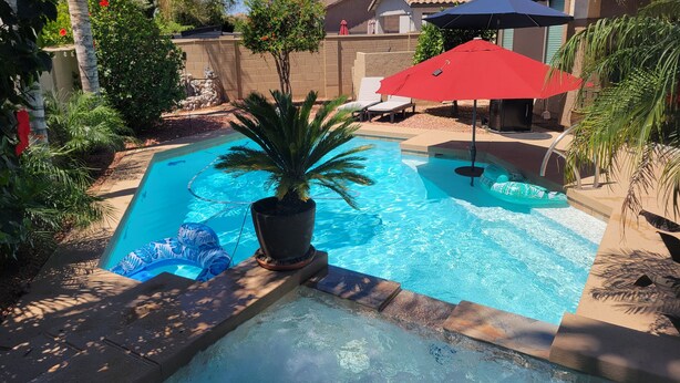Une piscine avec un jacuzzi, entourée de palmiers et agrémentée d’un parasol rouge.