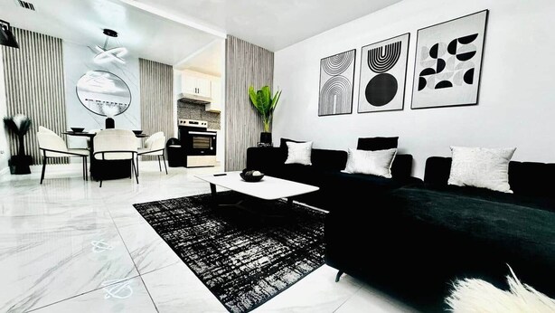 Una sala de estar moderna con un sofá negro, una mesa de centro y un comedor con mesa y sillas.