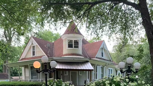 Uma casa em estilo vitoriano com varanda em volta, uma torre e um grande jardim com hortênsias brancas.