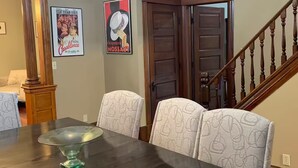 Uma sala de jantar com uma mesa de madeira escura, cadeiras estampadas, um candelabro e um cartaz na parede.