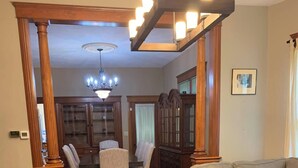 Uma sala de estar ampla com piso de madeira, um sofá grande, uma mesa de jantar com cadeiras e um lustre.