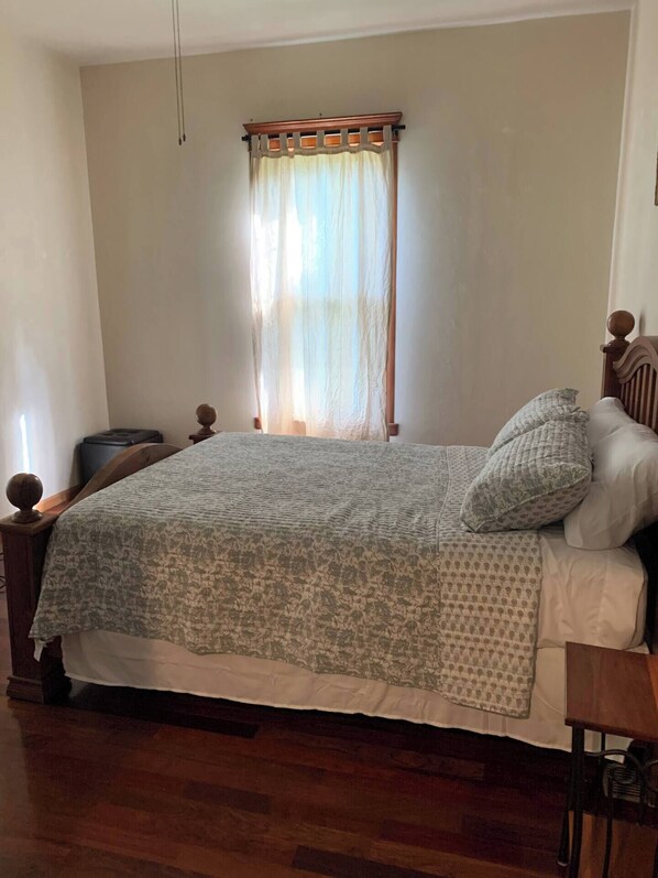 A bedroom with a wooden bed frame, a patterned bedspread, and a window with a wooden valance.