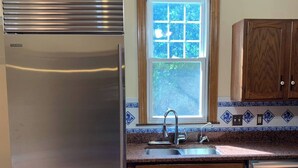 Uma cozinha com geladeira de aço inoxidável, armários de madeira, uma janela com vista e um revestimento de azulejos.