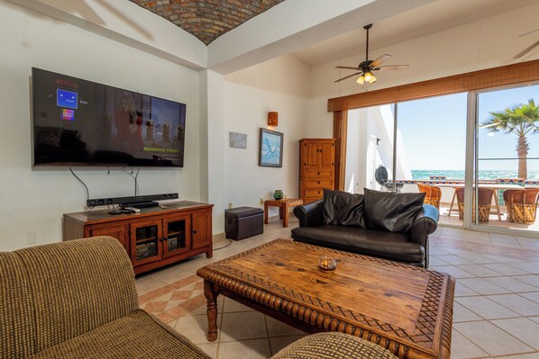 A living room with a television, sofa, coffee table, and a view of the ocean through large windows. - Las Palmas 14A 3 Bed 3.5 Bath By FMI Rentals (Puerto Peñasco)