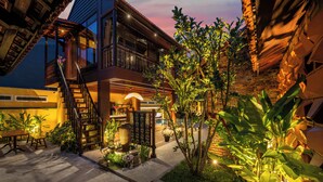 Un espacio exterior bien iluminado con una escalera que conduce a un balcón, rodeado de exuberante vegetación y plantas en macetas.