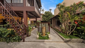 A courtyard with a central fountain, surrounded by lush greenery and a staircase leading to a balcony. - DEMIN VILLA HOI AN - Pool and BBQ Garden (Thanh pho Hoi An)