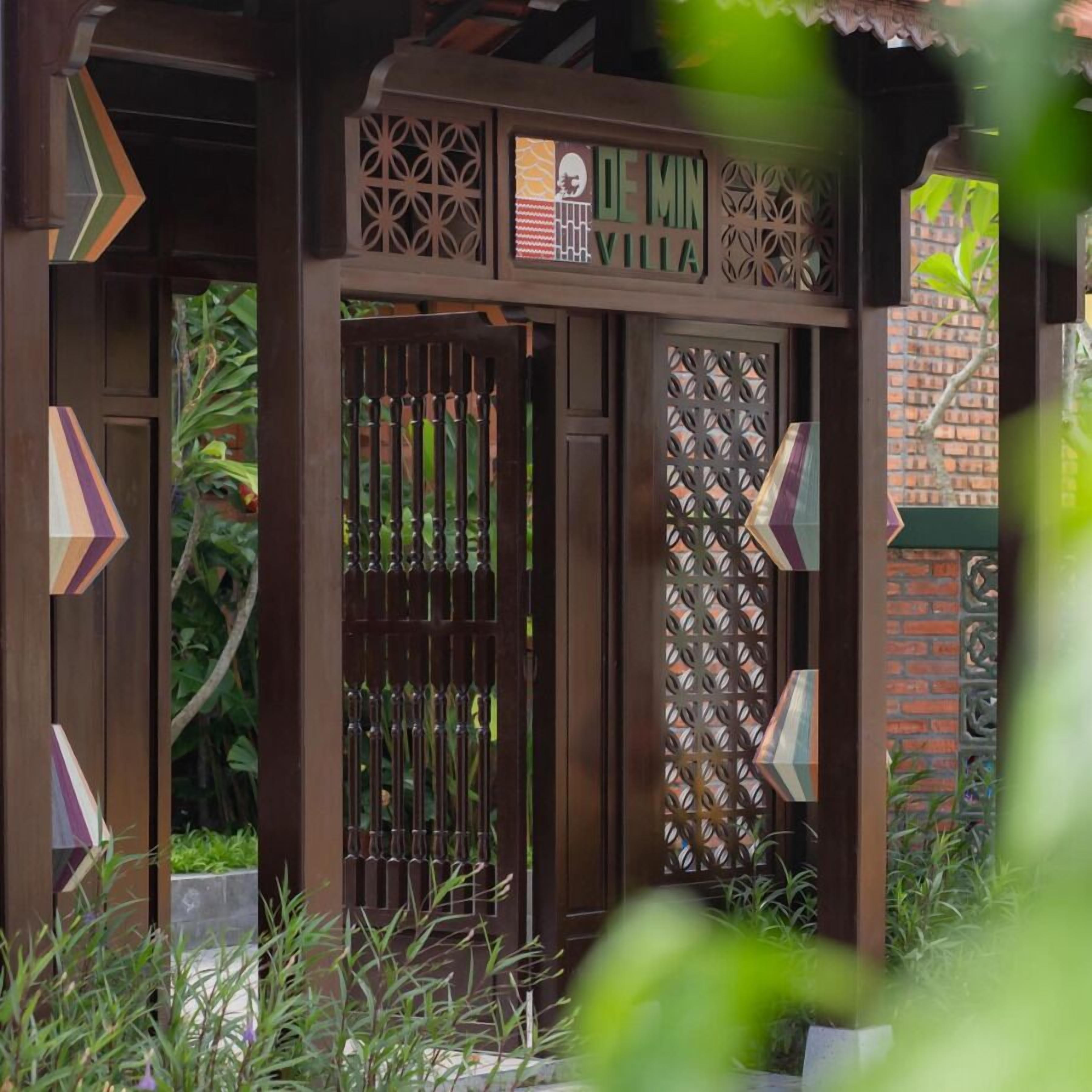 A wooden gate with decorative patterns and the text "DE MIN VILLA" above it.